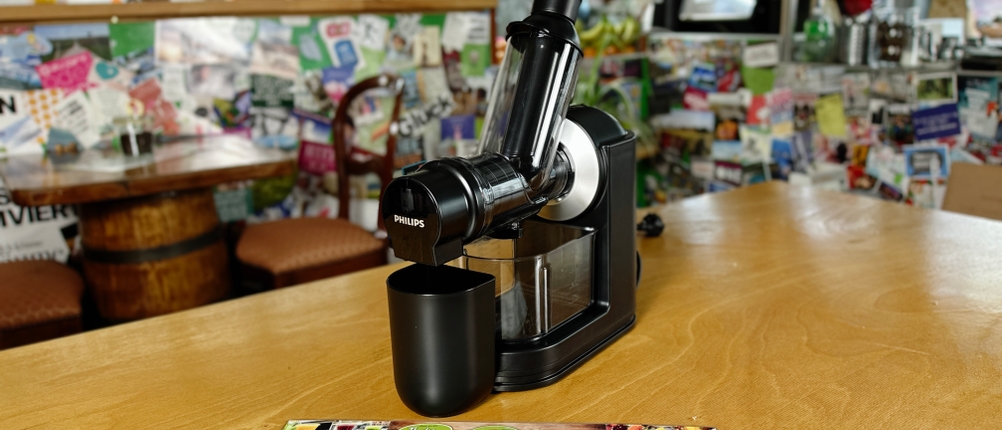 Der Philips HR1889/70 Slow Juicer mit seinen Zubehörteilen. Das Gerät und die mitgelieferten Behälter sind auf einem Tisch platziert.