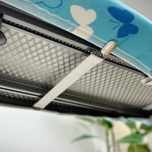 Die Rückseite des Bügeltischbezugs zeigt einen gespannten Gummistreifen mit Clipverschluss. Der Gurt ist zwischen den Metallstreben fixiert.