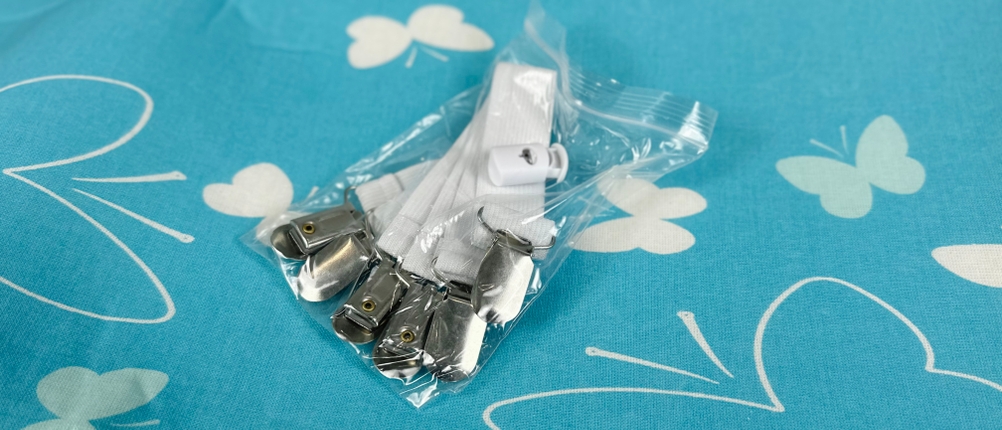 Zubehör für den arteneur Bügeltischbezug liegt auf dem Bezug. Das Set enthält Gummibänder mit Metallclips und Kordelzug.