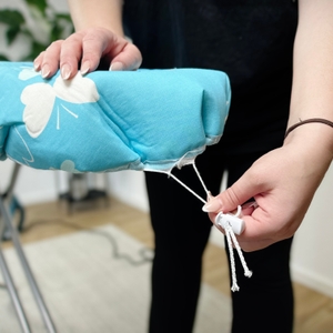 Eine Person zieht die Kordelschnur des Bügeltischbezugs an. Der Stopper ist bereits befestigt.