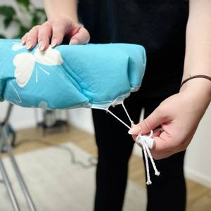 Eine Person zieht die Kordelschnur des Bügeltischbezugs an. Der Stopper ist bereits befestigt.