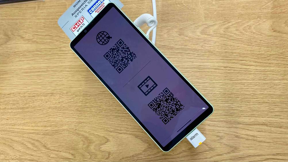 Auf einer Holzfläche befindet sich ein gesichertes Smartphone mit 6 Zoll im Test mit Label darüber.