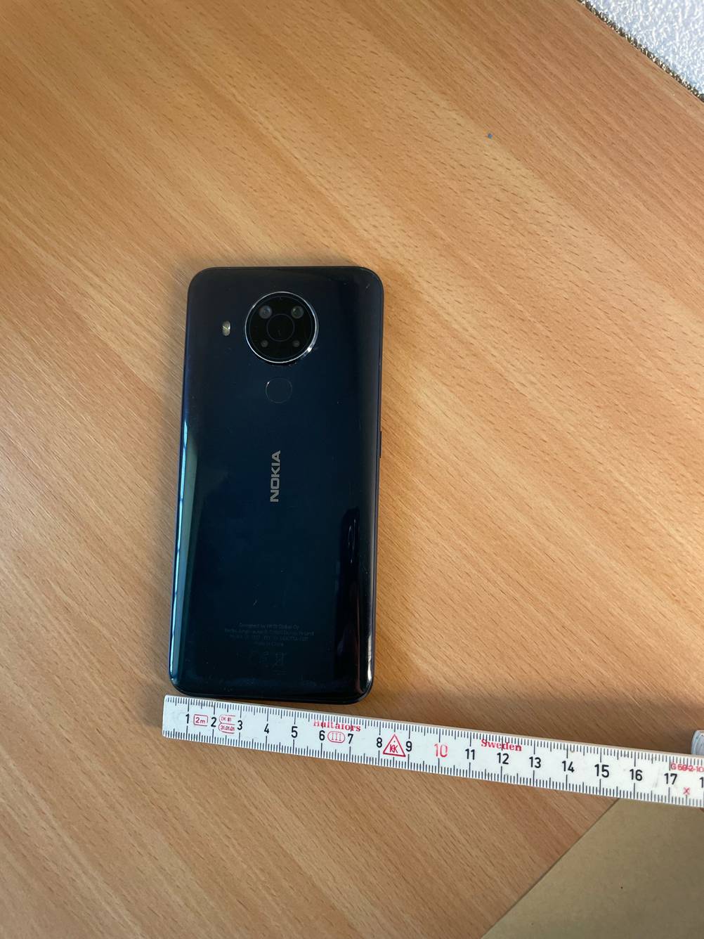 Getestet: Ein Smartphone bis 300 Euro mit der Rückseite nach oben, an der unteren Kante ein Meterstab.