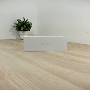 Die Schachtel mit der Apple Watch Series 11 steht auf einem Holztisch.