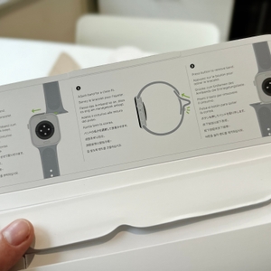 Die Person hält die geöffnete Verpackung der Apple Watch Series 11 in der Hand, und grundlegende Anweisungen zur Einrichtung der Uhr sind sichtbar.