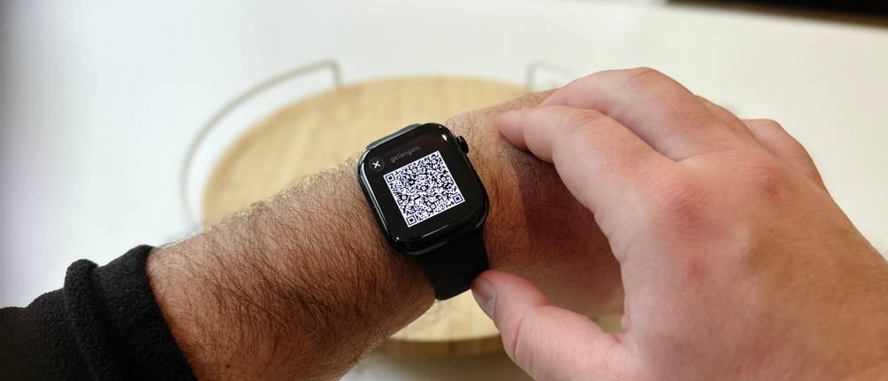 Die Person trägt die Apple Watch Series 11 am linken Handgelenk und demonstriert ihre Tragefähigkeit. Auf dem Bildschirm ist ein QR-Code sichtbar, der zum Koppeln der Smartwatch mit dem Telefon nützlich ist.