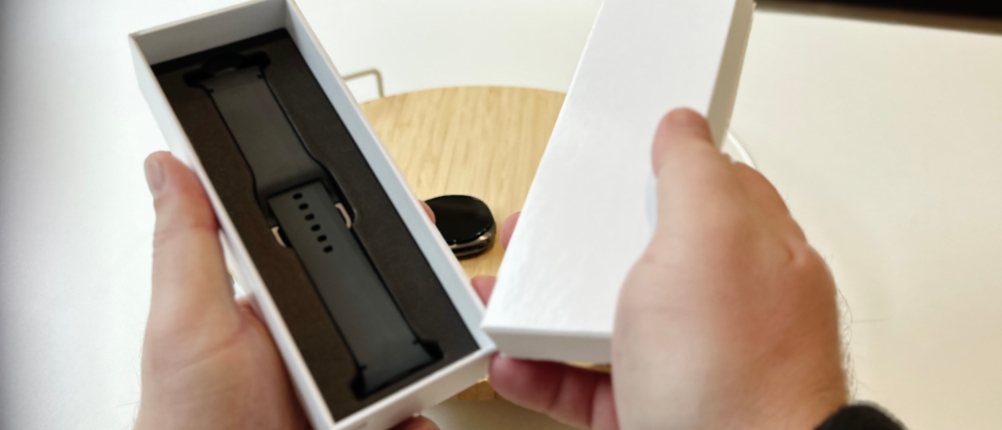 Die Person zeigt den Inhalt der Verpackung der Samsung-Galaxy-Watch-8-Smartwatch, einschließlich Armband und Bedienungsanleitung.