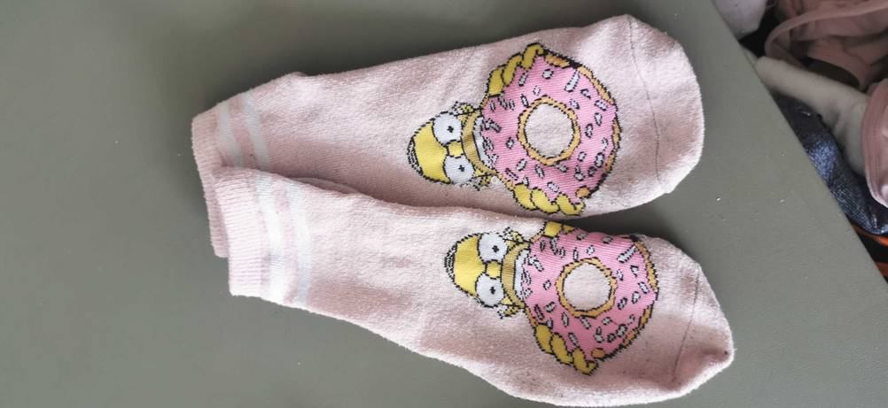 Ein paar rosa, getestete Sneaker-Socken mit niedlicher Verzierung liegen ausgebreitet auf einer grauen Oberfläche.