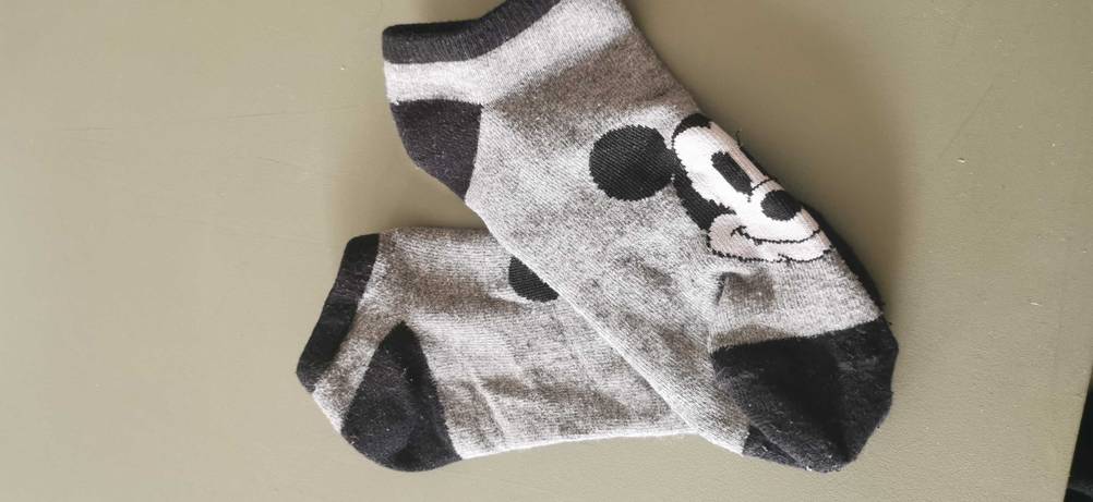 Ein Paar getestete Sneaker-Socken mit Micky Maus Motive liegen ausgebreitet übereinander auf einer grauen Oberfläche.