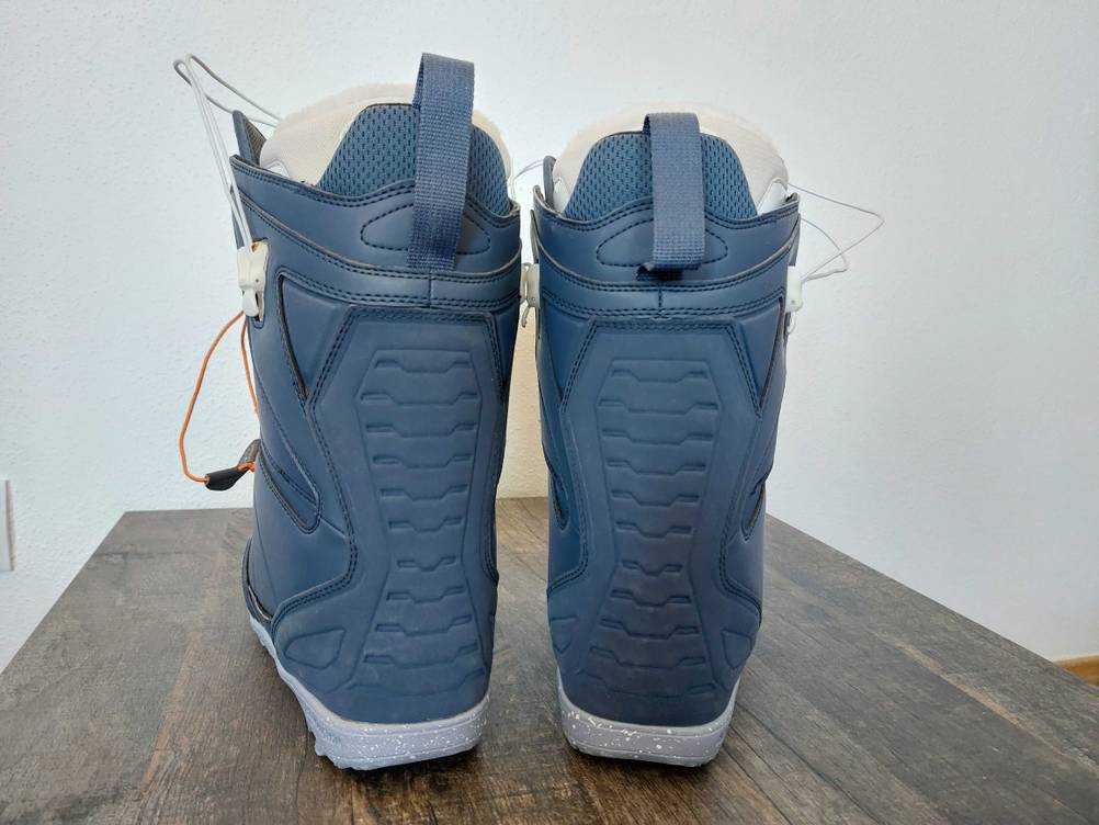 Ein Paar der getesteten Snowboard-Boots in blau von hinten auf einer Holzfläche.
