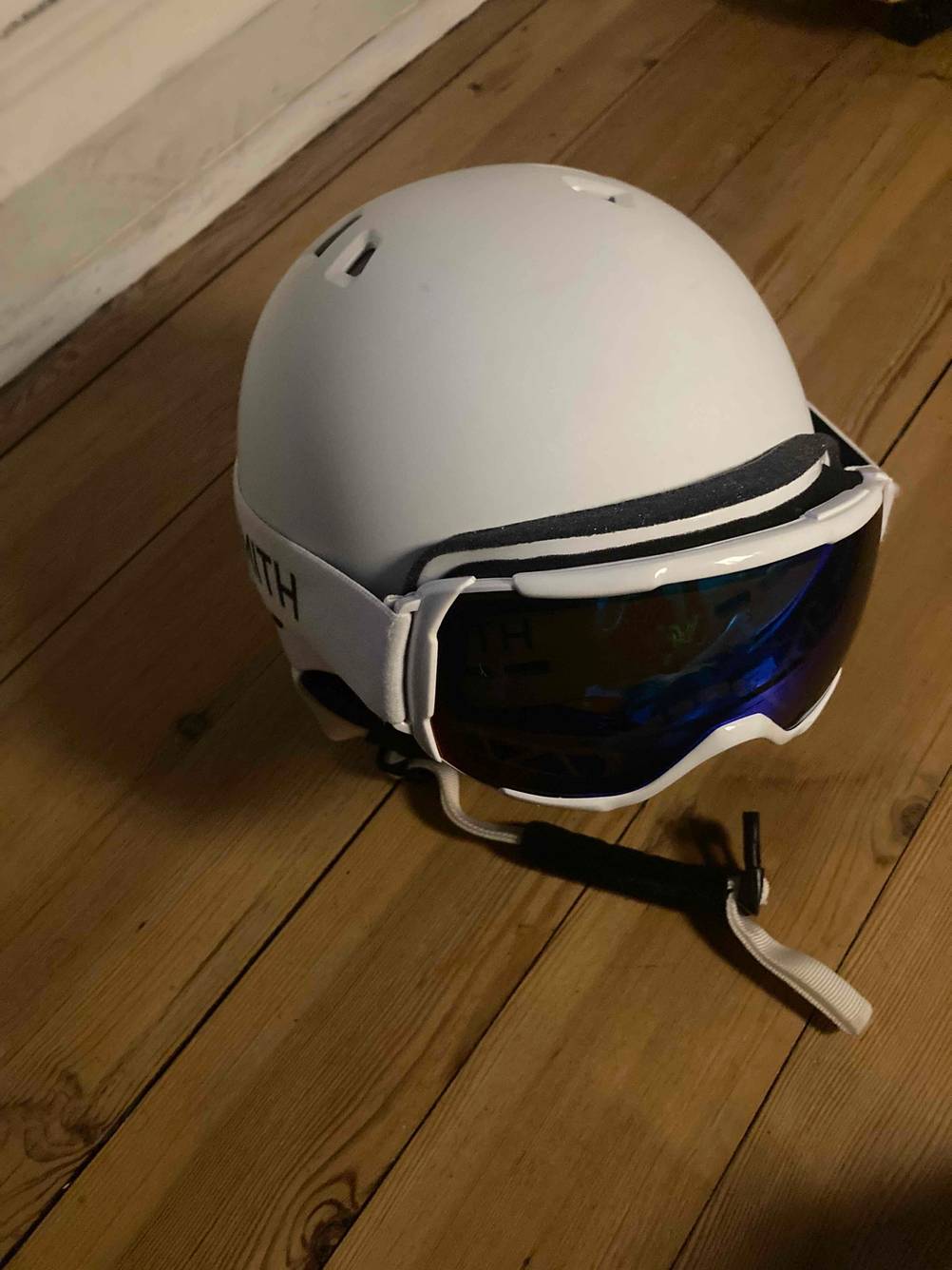 Ein Snowboardhelm im Test mit Brille auf einem Holzboden.