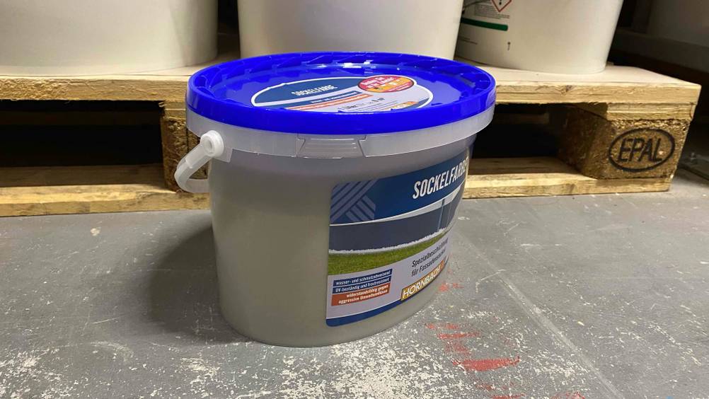 Ein Kanister der getesteten Sockelfarbe von der Seite auf einem Betonboden.