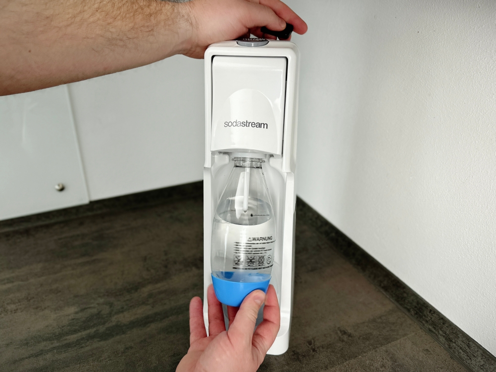 Eine Hand setzt eine Kunststoffflasche in den SodaStream Cool Sprudler ein.