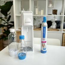 Der SodaStream Cool mit zwei PET-Flaschen und einem CO₂-Zylinder auf einem weißen Tisch.