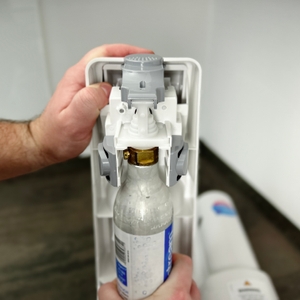 Eine Hand setzt einen klassischen Schraub-CO₂-Zylinder in den SodaStream Cool ein.