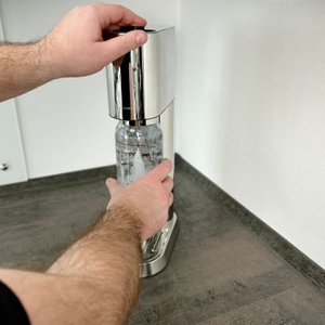Eine Person betätigt den oberen Hebel des SodaStream Enso, um Sprudelwasser zu erzeugen.