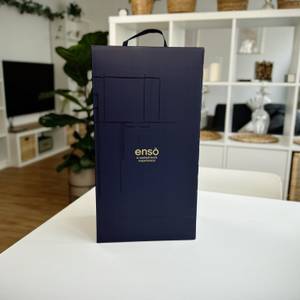 Eine stilvolle, dunkelblaue Verpackung des SodaStream Enso mit goldenem Schriftzug steht auf einem Tisch vor einem modernen Wohnbereich.