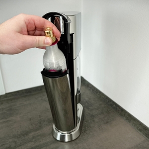 Eine Hand setzt einen CO₂-Zylinder in den SodaStream Enso Sprudler ein.