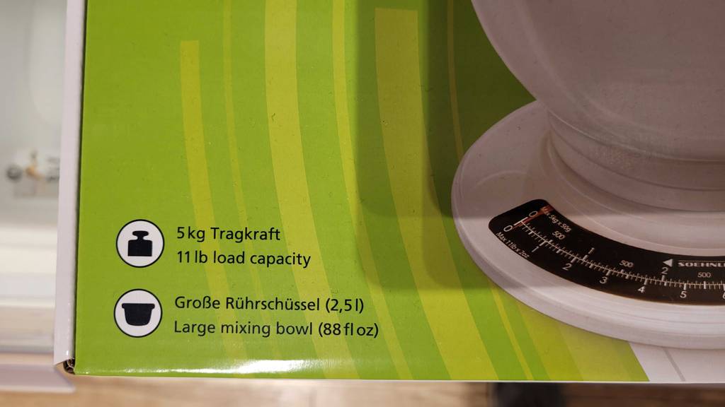 Hellgrüne Ecke der Verpackung einer weißen, analoge Küchenwaage im Test, mit Fokus auf die Informationen: große Rührschüssel, 5 kg Tragkraft.