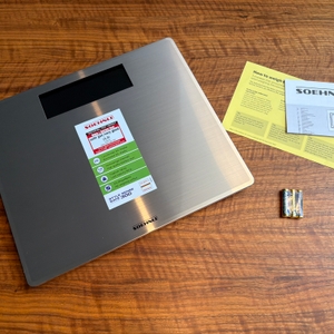 Der Lieferumfang der Soehnle Style Sense Safe 300 steht auf einem Holztisch.