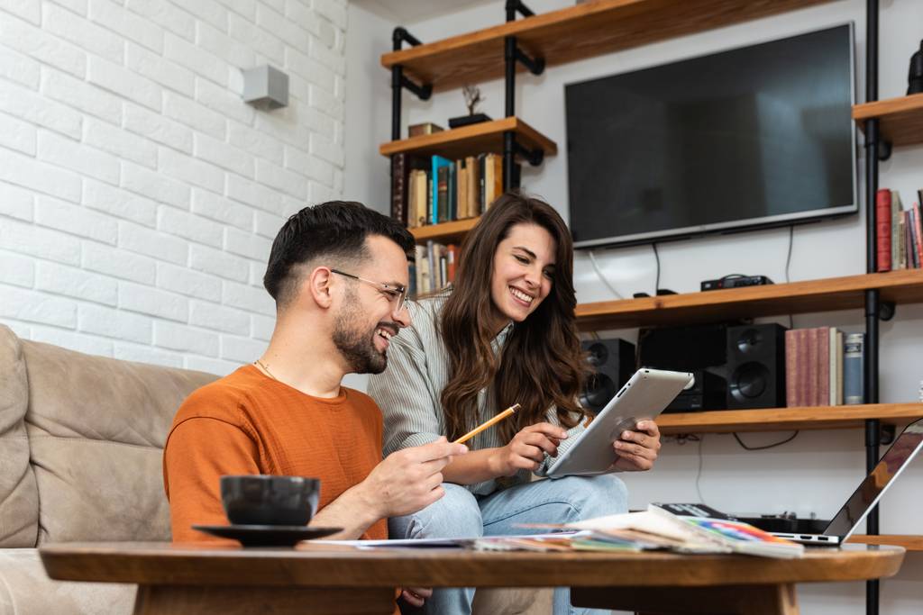 Sofortkredite im Vergleich: Ein junges Paar sitzt im Wohnzimmer und schaut lächelnd auf ein Tablet.