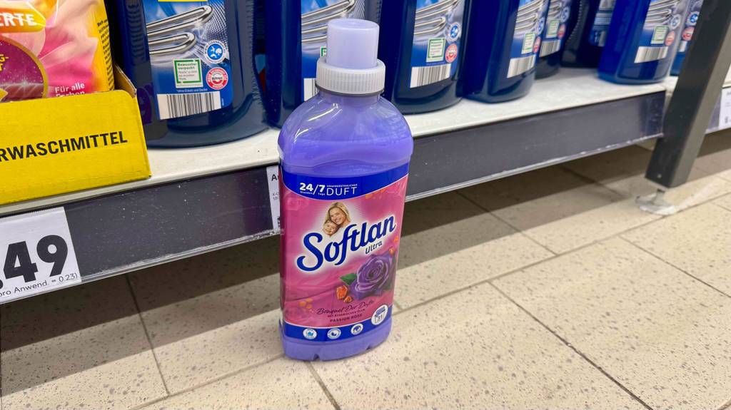 Eine Flasche Softlan Weichspüler steht zum testen auf einem Fliesenboden vor einem Regal mit anderen Produkten.