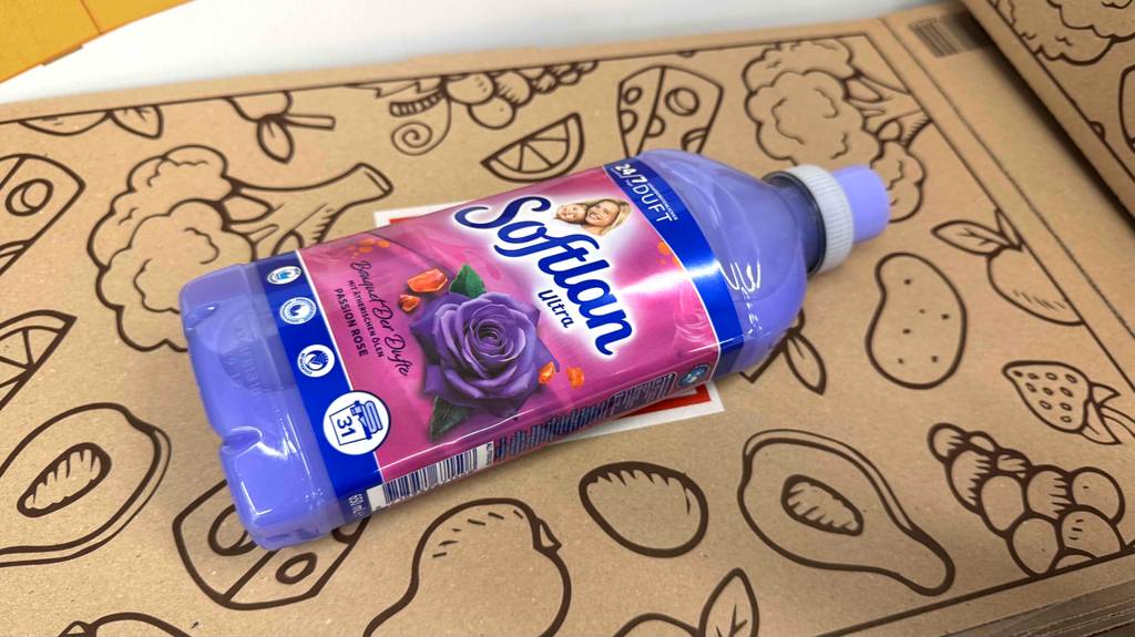 Eine Flasche getesteter Softlan Weichspüler liegt auf einem Karton mit Lebensmittelsymbolen.