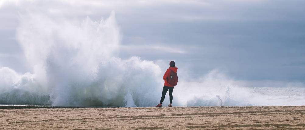 Stoftshelljacke-Damen-Test: Eine Frau in einer roten Softshelljacke am Meer. 