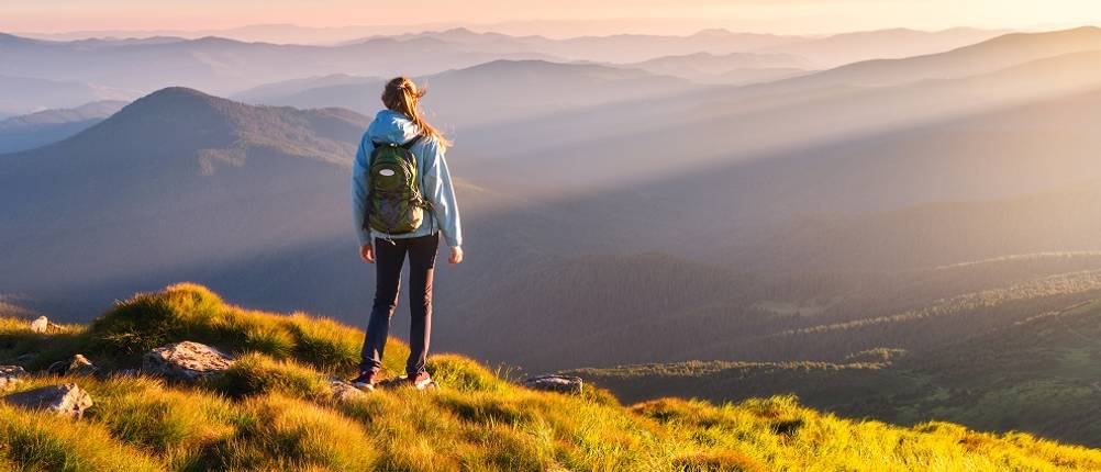 Softshelljacke-Damen-Test: Eine Frau mit einem Rucksack schaut auf Berge. 