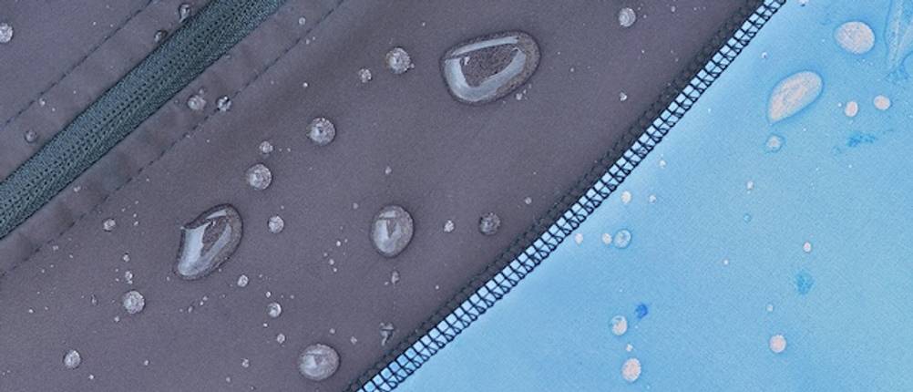 Softshelljacke für Herren im Test: Nahaufnahme von Wassertropfen die auf einer blauen Softshelljacke abperlen.