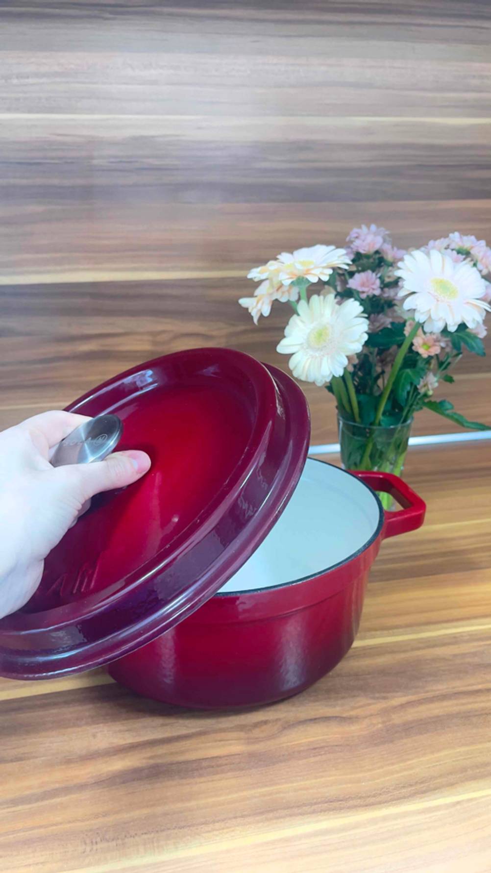 Gusseisen-Topf mit 24 cm-Test: Eine Hand nimmt den Deckel ab.