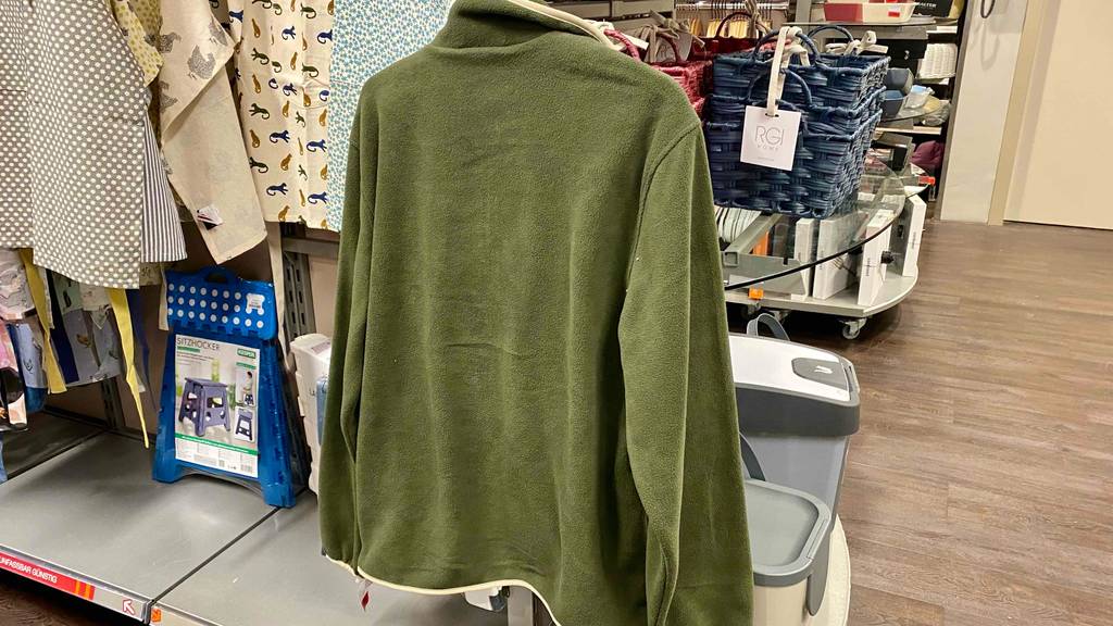 Ansicht von hinten auf eine Fleecejacke für Herren im Test: Das olivgrüne Modell befindet sich hängend in einem Geschäft.