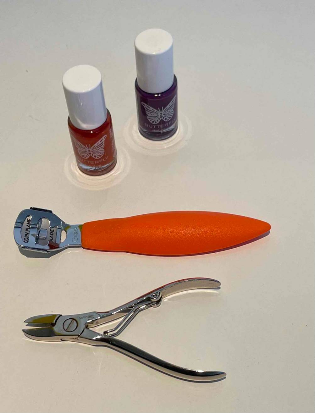 Eine getestete Fußnagelzange liegt geschlossen unterhalb weiteren Pediküre-Produkten geschlossen auf einem hellen Untergrund.
