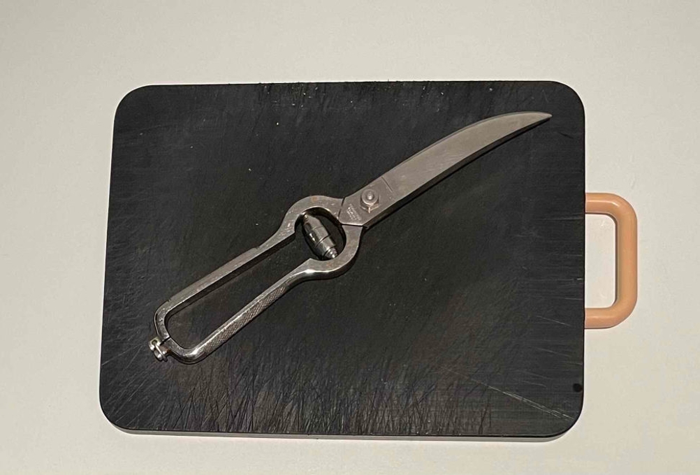 Getestete Geflügelschere liegt geschlossen auf einem schwarzen Brett mit Holzgriff.