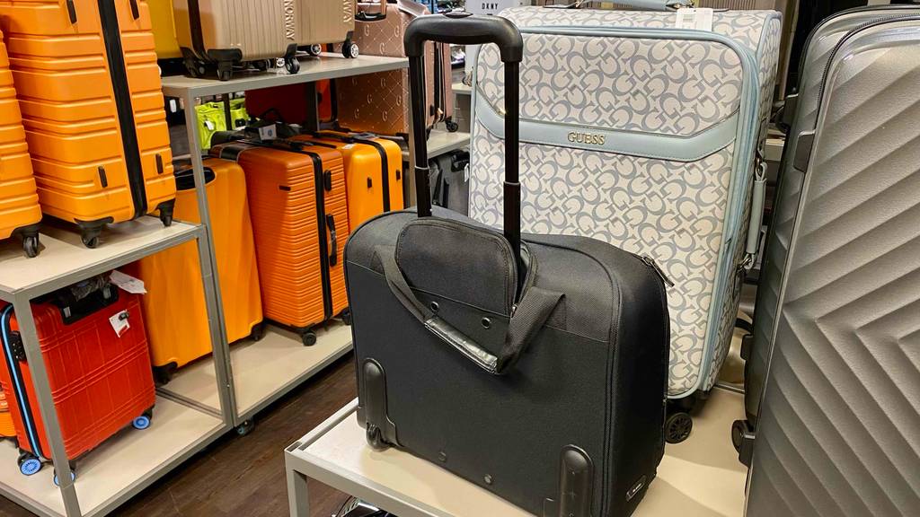 Pilotenkoffer getestet: Ein Modell aus schwarzem Gewebe steht mit verlängertem Griff auf einem Regal in einem Koffergeschäft.