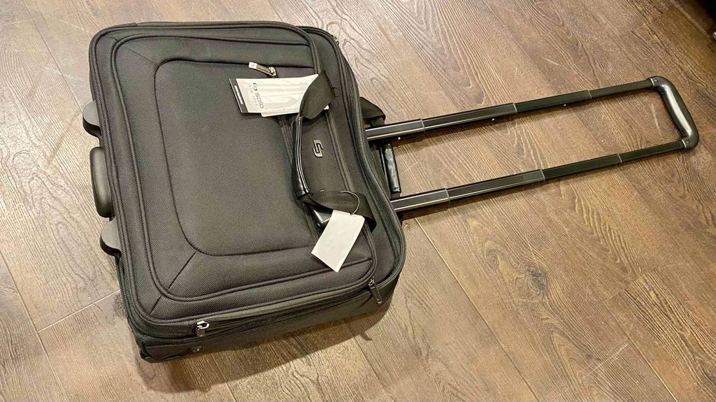 Ein getesteter Pilotenkoffer aus schwarzem Gewebe liegt mit ausgezogenem Griff auf einem Holzboden.