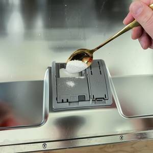 Mit einem Löffel wird eine kleine Menge Spülmaschinenpulver von Somat in das Fach der Maschine eingefüllt.