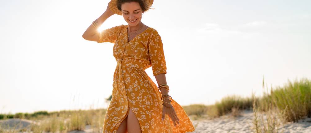 Sommerkleid-Test: Eine Frau mit Hut und gelbem Sommerkleid läuft über Sand.