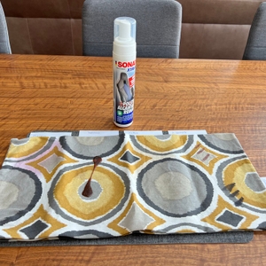 Ein Kissenbezug mit einigen Verschmutzungen liegt vor dem Sonax XTREME Polsterreiniger.