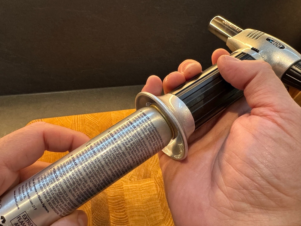 Eine Hand hält eine Butangasflasche an die Unterseite des Sondiko-Küchenbrenners S400