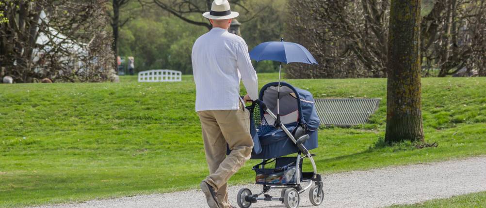 Sonnenschirm Kinderwagen Test: Mann schiebt Kinderwagen mit Sonnenschirm im Park