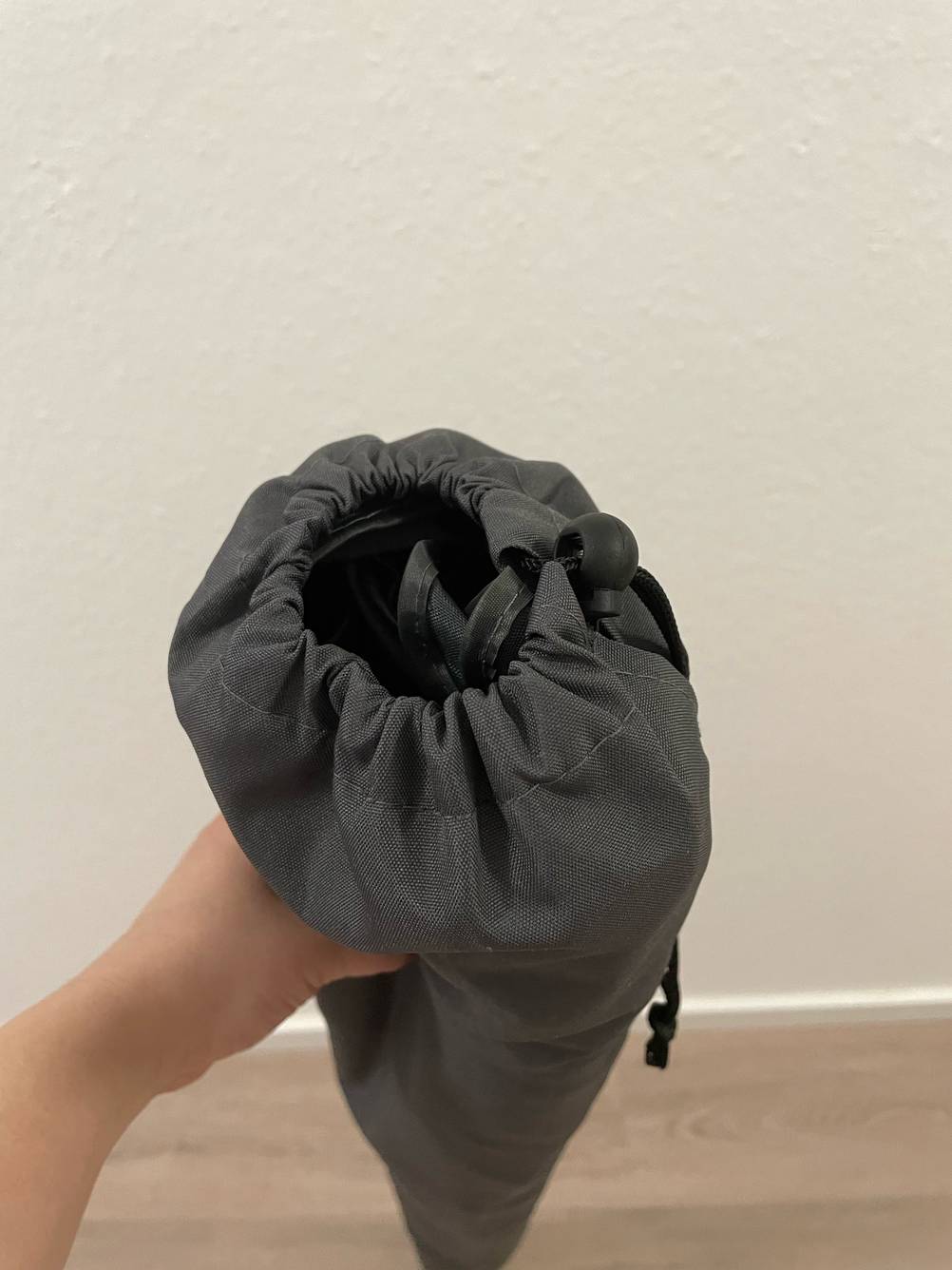 Eine Hand hält einen in der Aufbewahrungstasche verstauten getesteten Sonnenschirm knickbar.