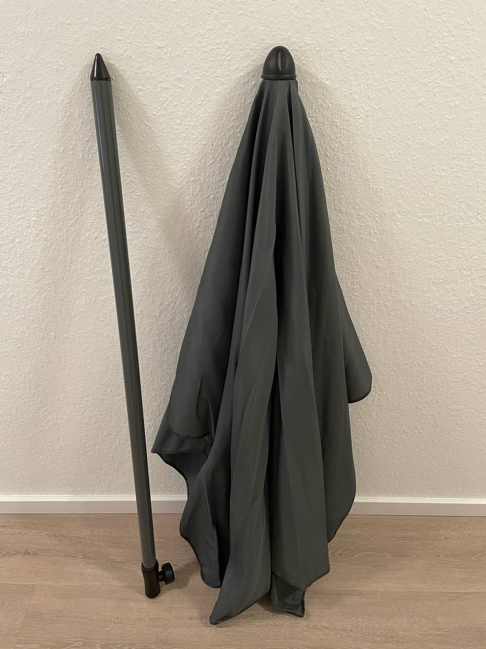 Ein Sonnenschirm knickbar lehnt zum testen an einer weißen Wand.