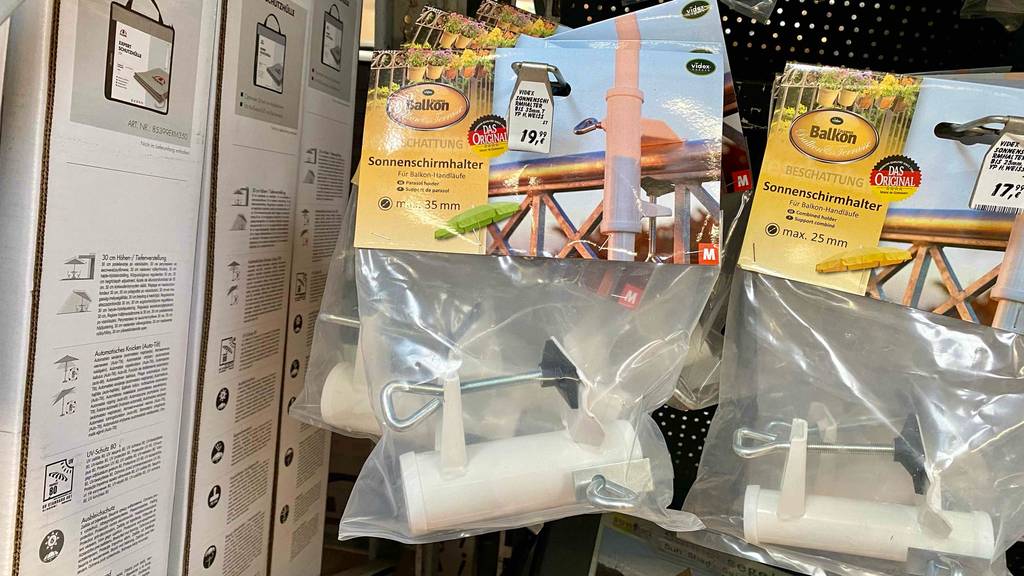 Mehrere getestete Sonnenschirmhalter für Balkongeländer befinden sich verpackt in einem Geschäftsregal. 