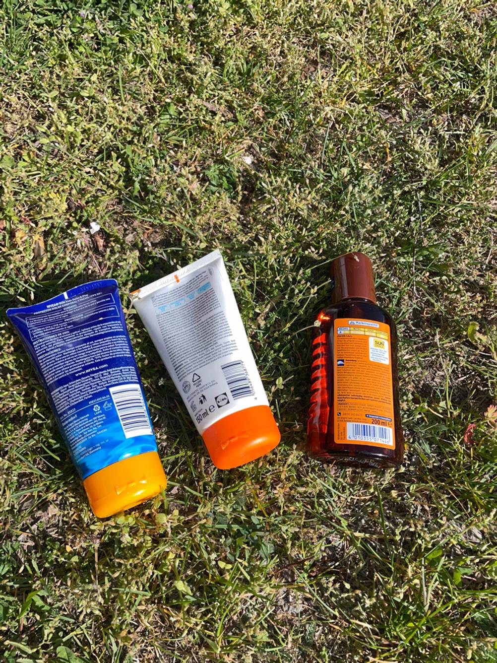 Sonnenschutzmittel getestet: Drei Flaschen mit der Rückseite nach oben auf einer Wiese.