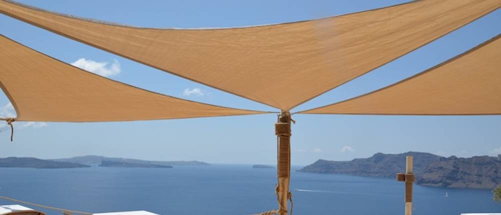Drei braune getestete Sonnensegel-Dreiecke über einer Terrasse mit Meerblick.