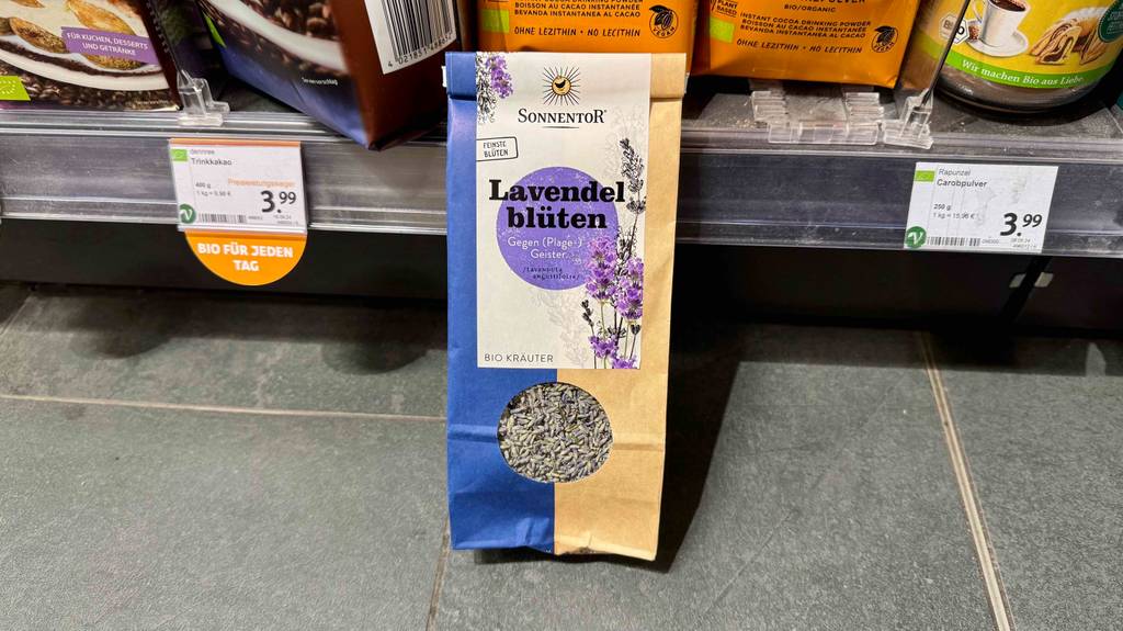 Im Test: getrocknete Lavendelblüten in einer Papiertüte befinden sich vor einem Regal mit Lebensmitteln.
