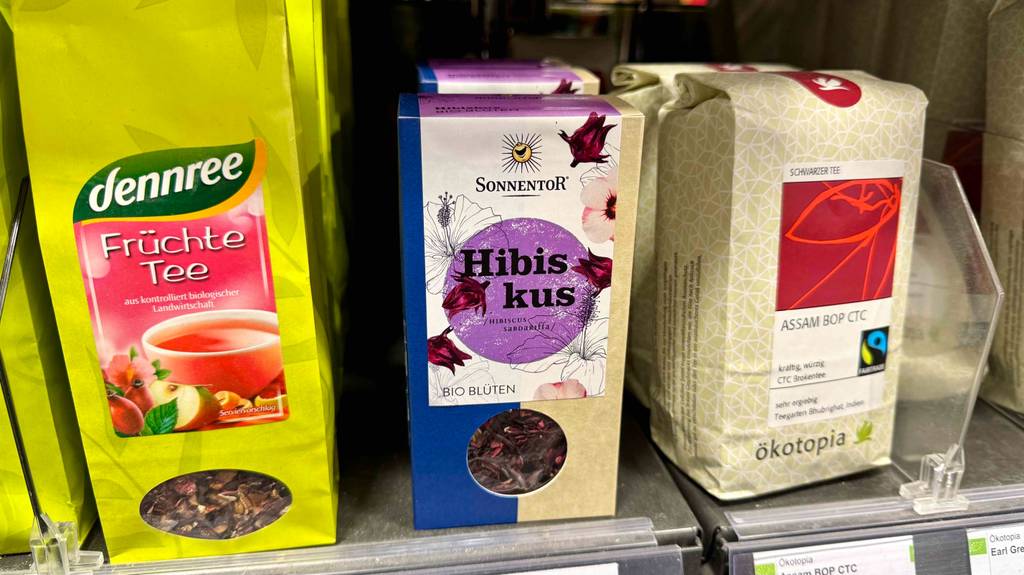 Im Test: Hibiskustee in der Verpackung mit losen Teeblättern steht zwischen anderen Teesorten in einem Verkaufsregal.