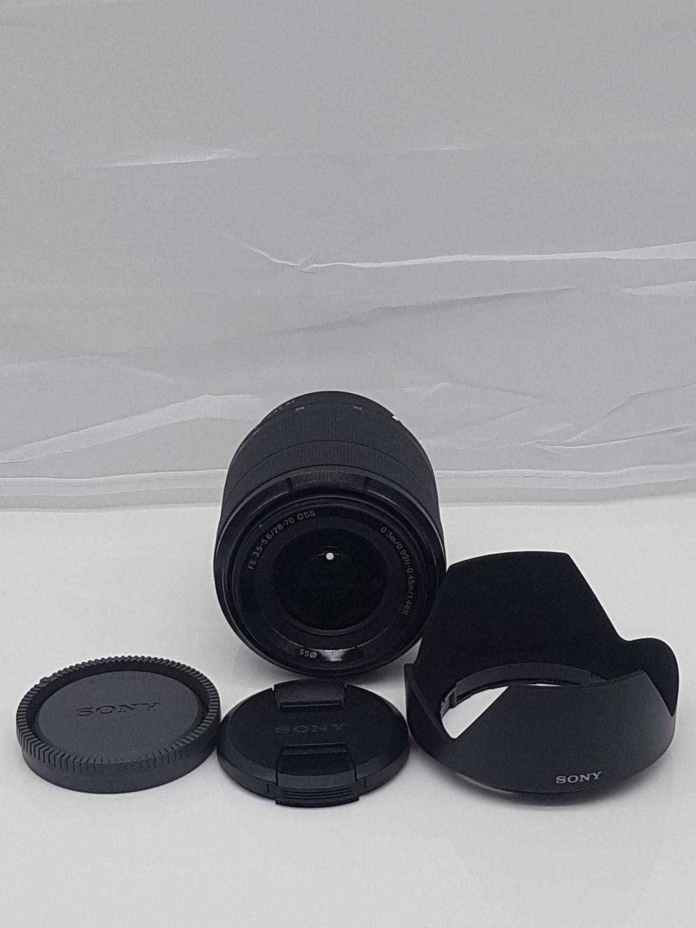 Ein getestetes Sony-E-Mount-Objektiv auf einer helleln Fläche von vorne, davor das mitgelieferte Zubehör.