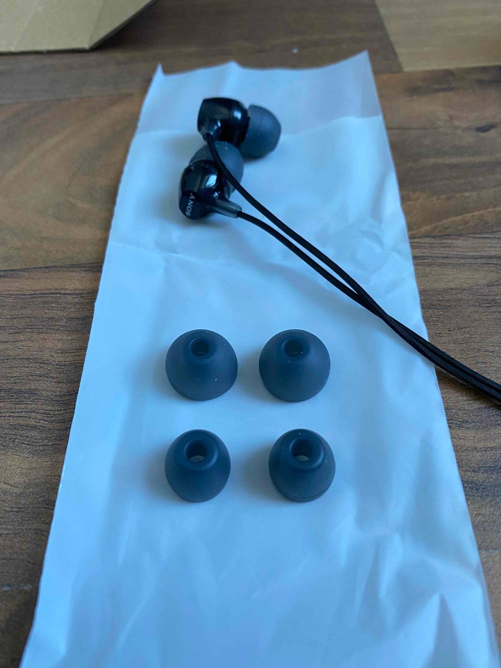 In-Ear Sony-Kopfhörer im Test liegen ausgepackt hinter zwei weiteren Ohrhörergrößen auf einer weißen Kunststofftüte.